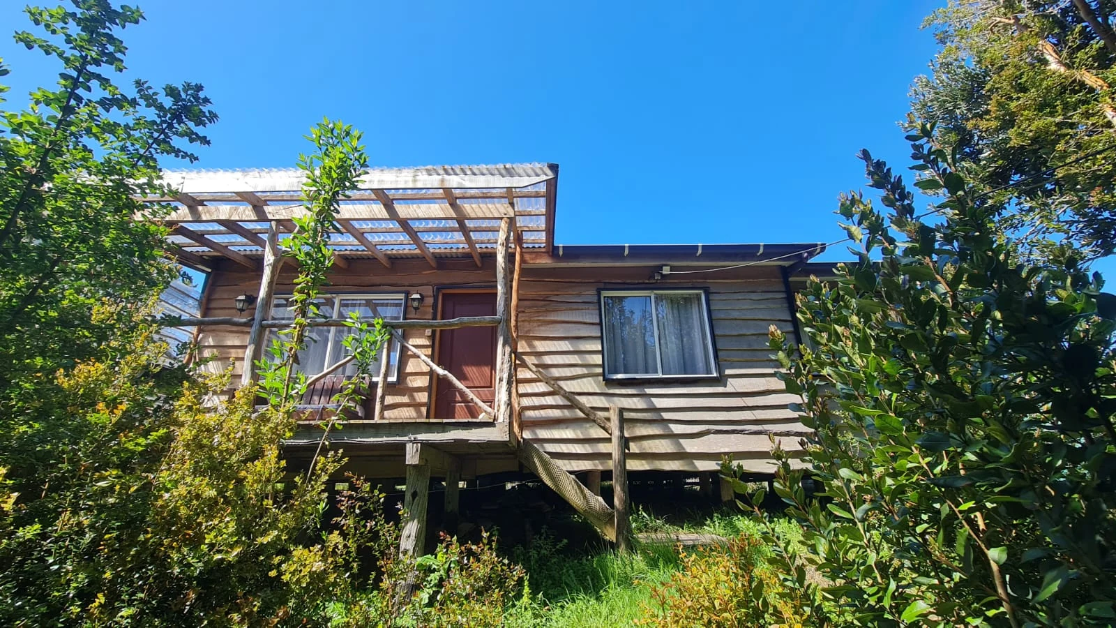 Fachada de una cabaña rústica rodeada de vegetación en Paraíso Wilkeco